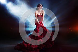 Beauty Brunette model woman in evening red dress. Beautiful fashion luxury makeup and hairstyle. Dark background, light