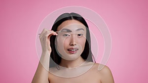 Beauty care concept. Young pretty asian woman with bare shoulders brushing her eyebrows, looking at camera like mirror
