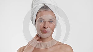 Beauty care. Well-groomed middle aged woman with towel on head caressing her smooth face, enjoying softness of her skin