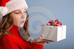 Beauty Christmas fashion model girl holding Xmas gift box. Beautiful lady, Long straight flying hair, red santa hat, holding gift