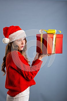 Beauty Christmas fashion model girl holding Xmas gift box. Beautiful lady, Long straight flying hair, red santa hat, holding gift