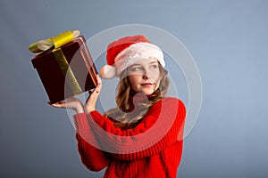 Beauty Christmas fashion model girl holding Xmas gift box. Beautiful lady, Long straight flying hair, red santa hat, holding gift