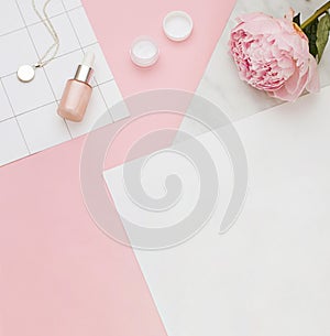 Beauty concept frame with peony flower and cosmetics bottles on the pink background. Top view.