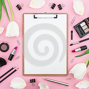 Beauty concept with white flowers, clipboard, cosmetics and accessory on pink background. Top view. Flat lay. Home feminine desk.