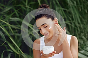 Beauty Concept. Woman Applying Cosmetics Cream, Spreads it on her face to moisturize her skin and Smiling.