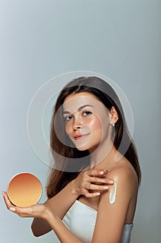 Beauty Concept. Woman holds a cosmetic crem in her hand and spreads it on her shoulder  to moisturize her skin.