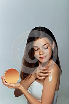 Beauty Concept. Woman holds a cosmetic crem in her hand and spreads it on her shoulder to moisturize her skin. Female Applying Cre