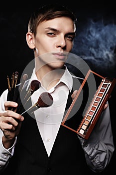 Beauty concept. Young male make up artist posing with make-up brushes and shadow palette