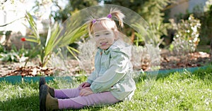 Beauty cute child girl in spring garden sitting on lawn. Smiling baby girl