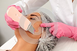 Beauty doctor with ultrasonic scraber doing procedure of ultrasonic cleaning of face. Cosmetology and facial skin care.