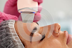 Beauty doctor with ultrasonic scraber doing procedure of ultrasonic cleaning of face. Cosmetology and facial skin care.