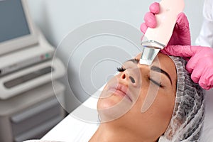 Beauty doctor with ultrasonic scraber doing procedure of ultrasonic cleaning of face. Cosmetology and facial skin care.