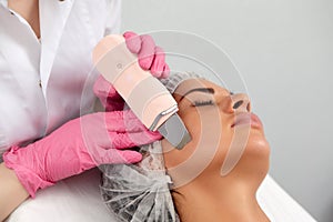 Beauty doctor with ultrasonic scraber doing procedure of ultrasonic cleaning of face. Cosmetology and facial skin care.