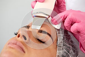 Beauty doctor with ultrasonic scraber doing procedure of ultrasonic cleaning of face. Cosmetology and facial skin care.