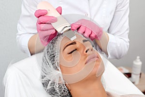 Beauty doctor with ultrasonic scraber doing procedure of ultrasonic cleaning of face. Cosmetology and facial skin care.