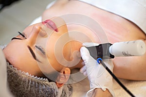 Beauty doctor with ultrasonic scraber doing procedure of ultrasonic cleaning of female client& x27;s neck