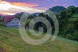 The beauty of the evening sky above the peaks of the hills and the treetops. With green slopes and rural houses standing