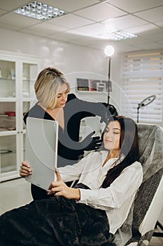 Beauty expert is holding mirror and showing result of drawn eyebrows to the client. Eyebrows microblading concept