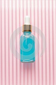 Beauty face oil in blue glass dropper bottle om pinke background. Trendy shoot of cosmetics packaging. Essential oil with natural