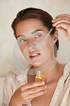 Beauty Face. Woman Applying Essential Oil On Facial Skin And Looking Away. Beautiful Model Moisturizing Derma.