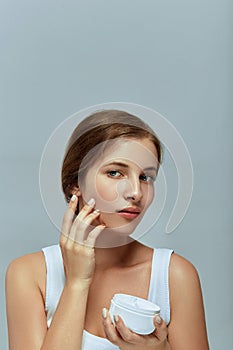 Beauty Facial Care. Female Applying Cream and Smiling. Portrait Of  Young Woman With Cosmetic Cream On Skin.