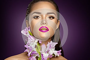 Beauty fashion brunette girl with gladiolus flowers. Glamour woman with perfect violet trendy makeup