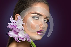 Beauty fashion brunette girl with gladiolus flowers. Glamour woman with perfect violet trendy makeup