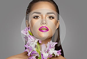 Beauty fashion brunette girl with gladiolus flowers. Glamour woman with perfect violet trendy makeup