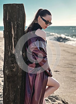 Beauty Fashion brunette model girl wearing stylish coat and sunglasses, posing on seaside