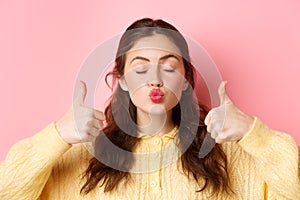 Beauty and fashion. Close up portrait of lovely and coy girl pucker lips with eyes closed, showing thumbs up in approval