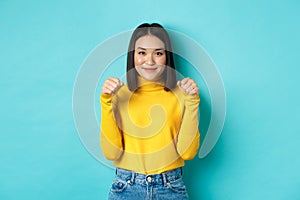 Beauty and fashion concept. Beautiful and stylish asian woman in yellow pullover, holding hands raised near chest as if