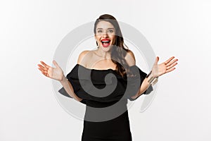 Beauty and fashion concept. Image of surprised and happy young woman in party dress reacting to good news, raising hands