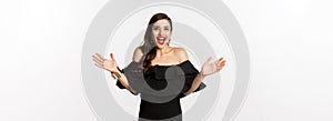 Beauty and fashion concept. Image of surprised and happy young woman in party dress reacting to good news, raising hands