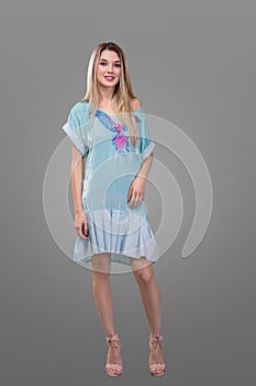 Beauty, fashion and happy people concept - young woman in blue dress with a parrot and high heels over grey background