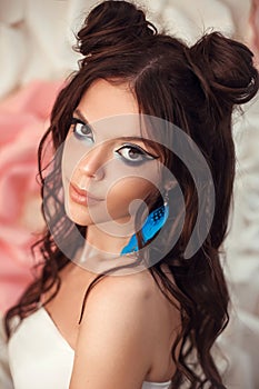 Beauty fashion model girl with creative art makeup and blue feather earring. Portrait of Beautiful brunette posing in studio,