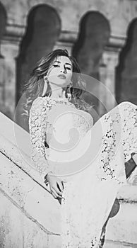 Beauty Fashion model girl. Fashion look. Girl in white dress sits on old stone handrails