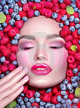 Beauty fashion model girl lying in fresh ripe fruits, berries and mint. Face in colorful berries close-up. Beautiful make-up