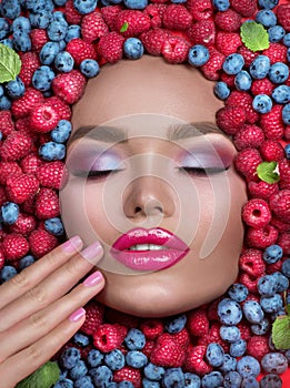 Beauty fashion model girl lying in fresh ripe fruits, berries and mint. Face in colorful berries close-up. Beautiful make-up