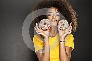 Beauty fashion model girl taking sweets and colorful donuts. Funny joyful Vogue styled woman with sweets on pink background. Diet