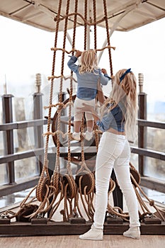 Beauty fashion mother with daughter family look. Beautiful blond woman playing with her little pretty blonde girl climb a rope by