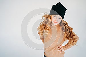 Beauty fashion portrait of smiling curly hair tween girl in black hat and beige sweater on the white background