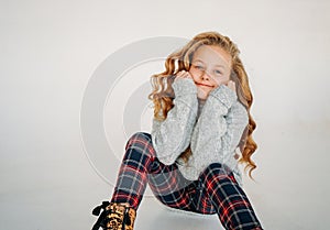Beauty fashion portrait of smiling curly hair tween girl in cozy knitted sweater and plaid pants on white background isolated