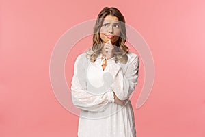 Beauty, fashion and women concept. Portrait of uncertain, serious-looking feminine young blond woman in white dress