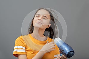 Beauty and fashion. A young Caucasian woman dries her hair with a hairdryer on a gray background
