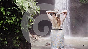 Beauty girl with healthy long hair outdoors. Happy young woman enjoying wild nature and power of waterfall. Beautiful