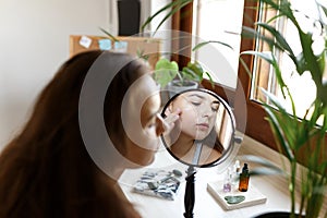 Beauty girl looking at mirror while touching her face and applying cream, wrinkles during morning beauty routine. Happy