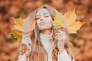 Beauty girl outdoors enjoying nature. Beautiful autumn female model holds an yellow leaf near the face. Fashion portrait