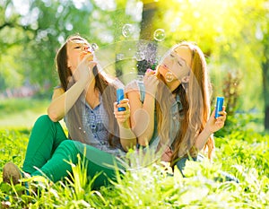 Beauty girls blowing soap bubbles in spring park