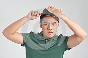 Beauty, grooming and people concept - smiling young man brushing hair with comb over gray background