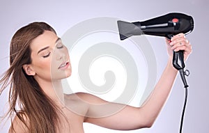 Beauty, hair dryer and a woman blowing her hairstyle in studio on a gray background for grooming or style. Salon